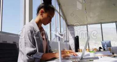 在<strong>现代</strong>办公室的<strong>办公桌</strong>上使用笔记本电脑的非裔美国女商人的侧视图